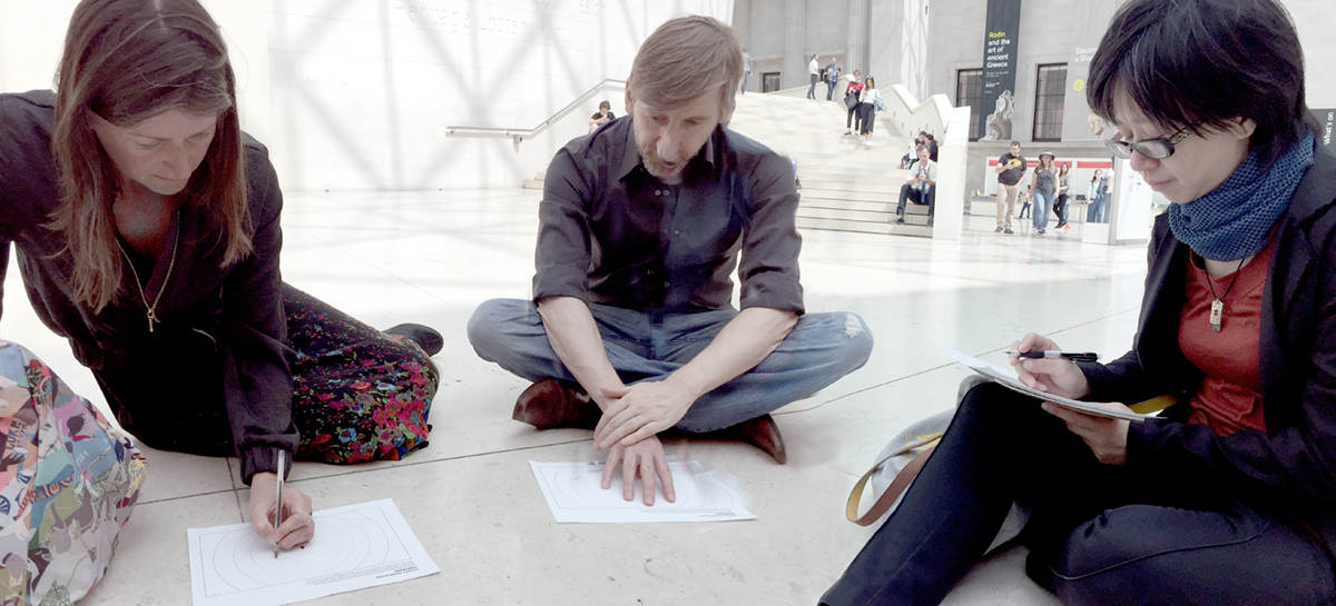 Students sit on the floor and take notes about what they are hearing.